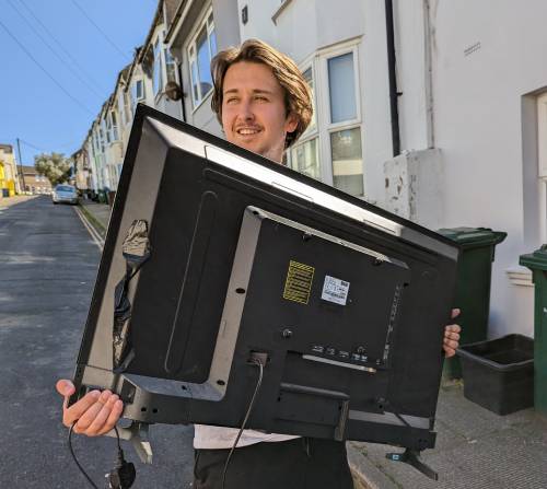 an image of danny knight, the founder and director of seaside removals, carrying a tv and whilst looking happy.